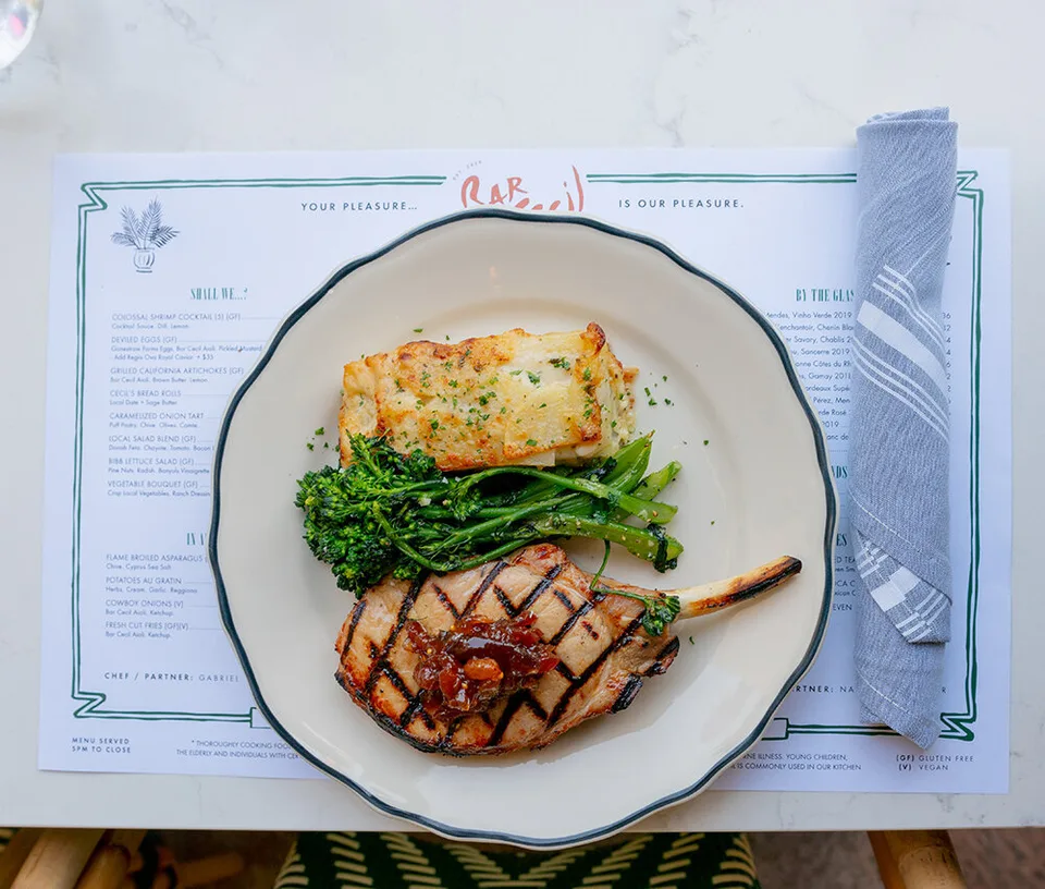 A grilled pork chop, potatoes au gratin, and broccolini served over a Bar Cecil menu.