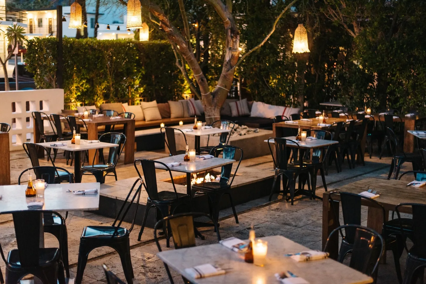 Candlelit tables surround a mature tree on Birba’s open-air patio at dusk.