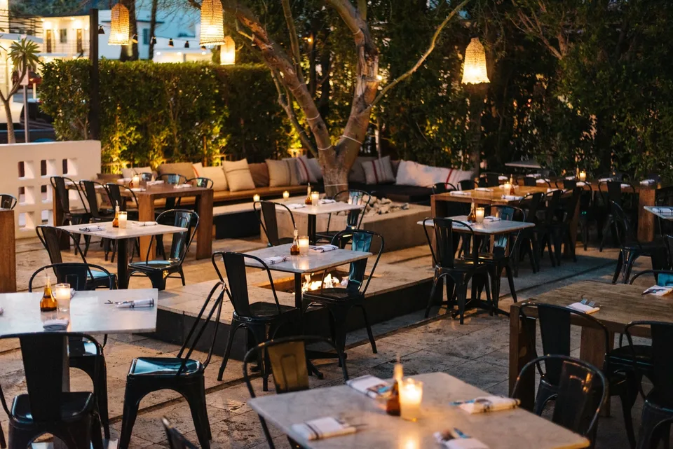 Candlelit tables surround a mature tree on Birba’s open-air patio at dusk.