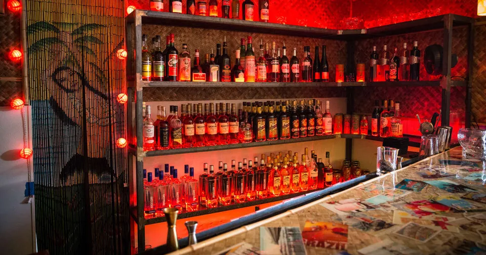 The back bar at Bootlegger Tiki glows red behind rows of spirits and a collage-covered bar top.
