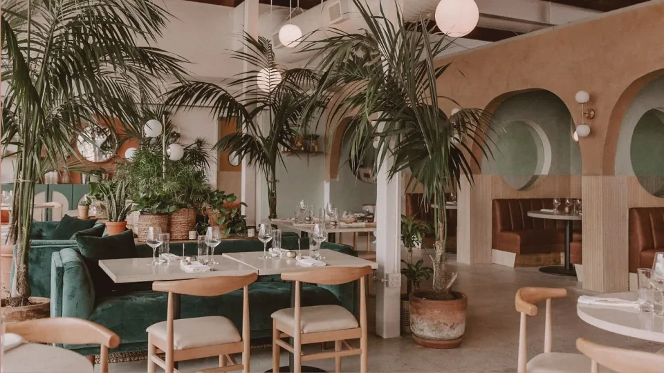 Boozehounds’ plant-filled dining room with green banquettes and arched booths.