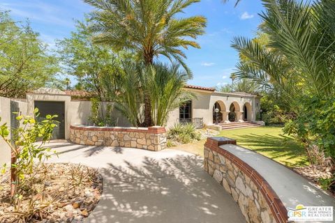 Garden-side exterior of Casa de Liberace with a Spanish tile roof, arched loggia, stone-and-brick walls, and palms.