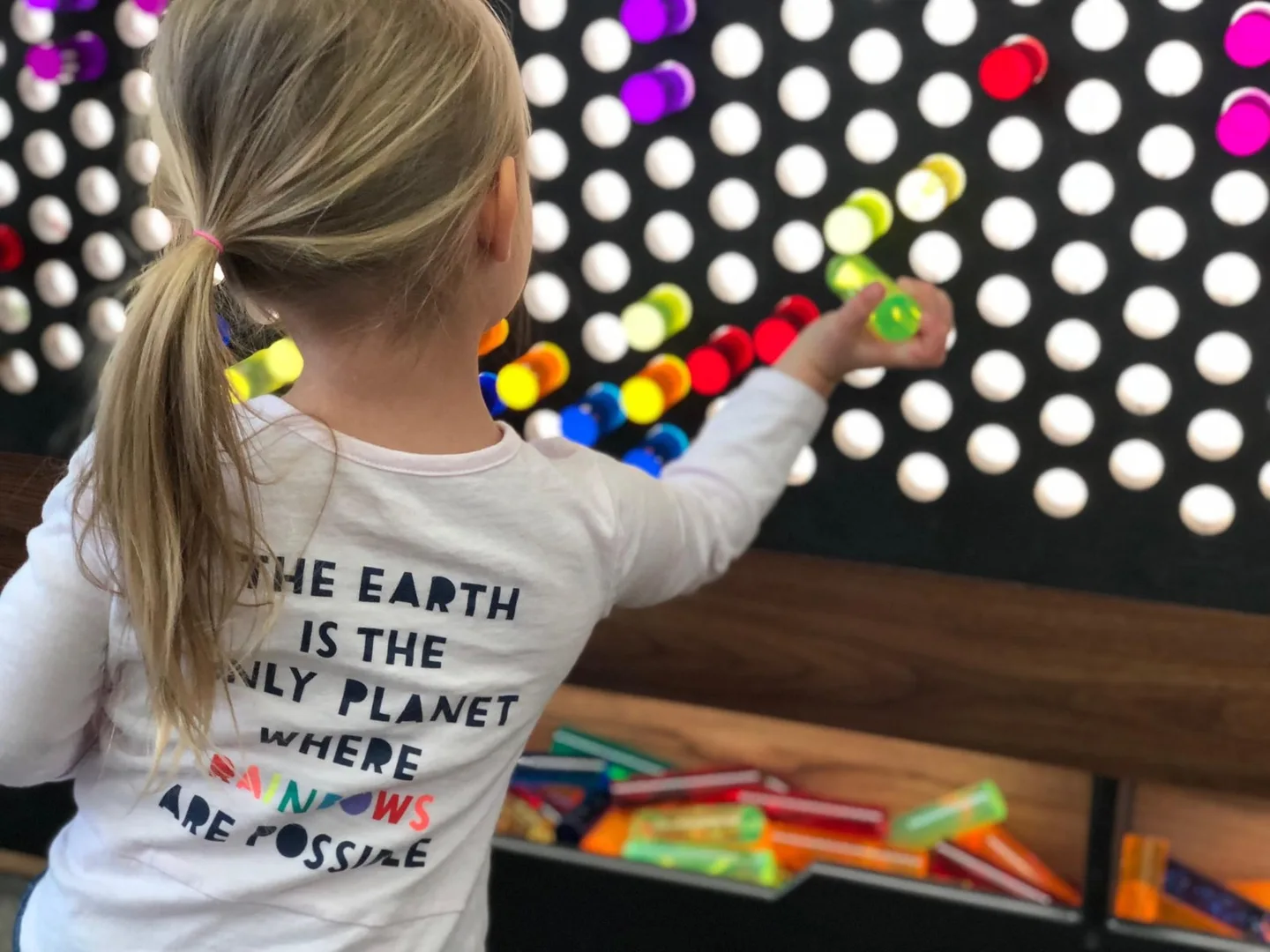 A child seen from behind places colorful pieces into the museum's illuminated LiteZilla wall.
