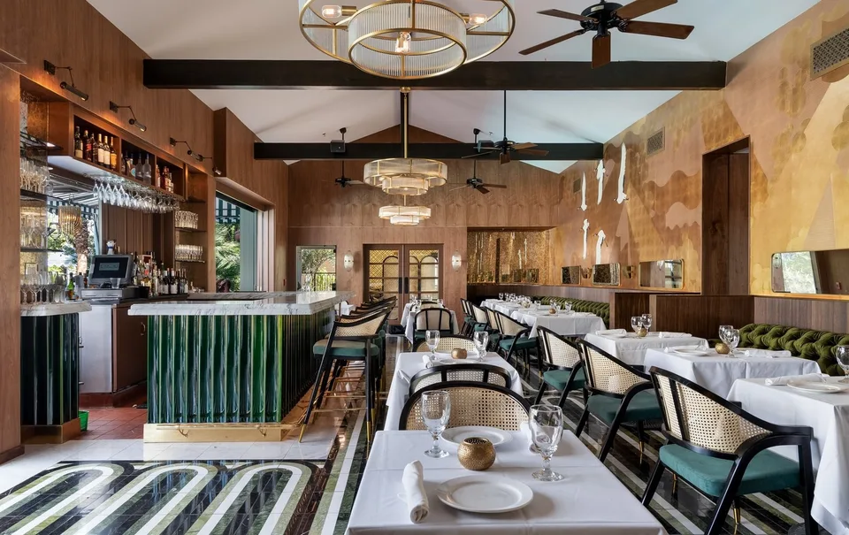The Colony Club dining room with a green-tiled bar, patterned floor, and white-clothed tables.