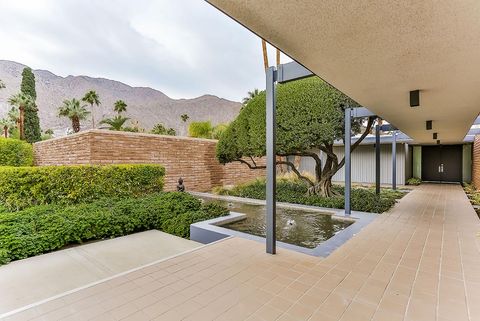 Covered entrance promenade of the Dinah Shore Residence with adobe walls, reflecting water, clipped trees, and mountains.