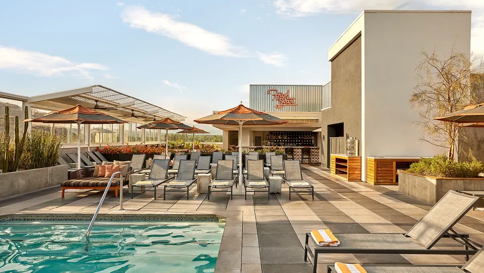 High Bar beside the rooftop pool at Kimpton Rowan Palm Springs with loungers, umbrellas, and mountain views.
