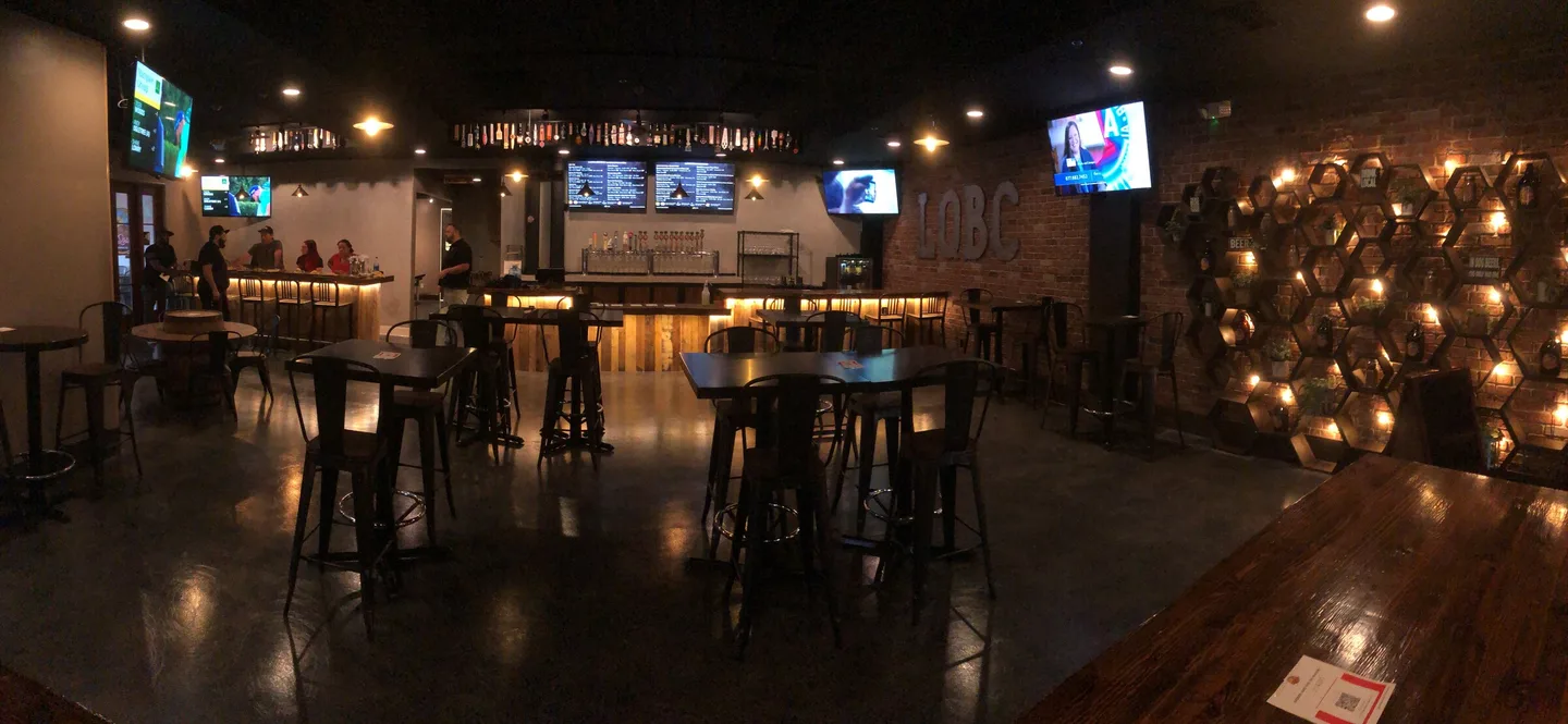 A warmly lit La Quinta Brewing taproom has a long bar, rows of tap handles, and tables arranged across the room.
