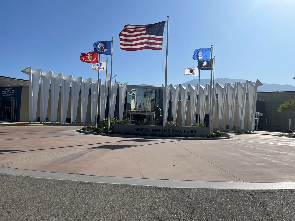 The Palm Springs Air Museum entrance displays flags and aircraft against a clear desert sky.