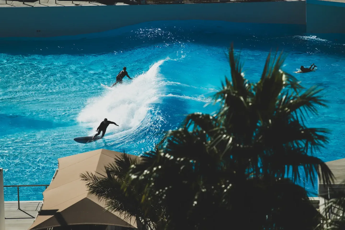 Two surfers ride opposite faces of an engineered A-frame wave while another surfer paddles at Palm Springs Surf Club.