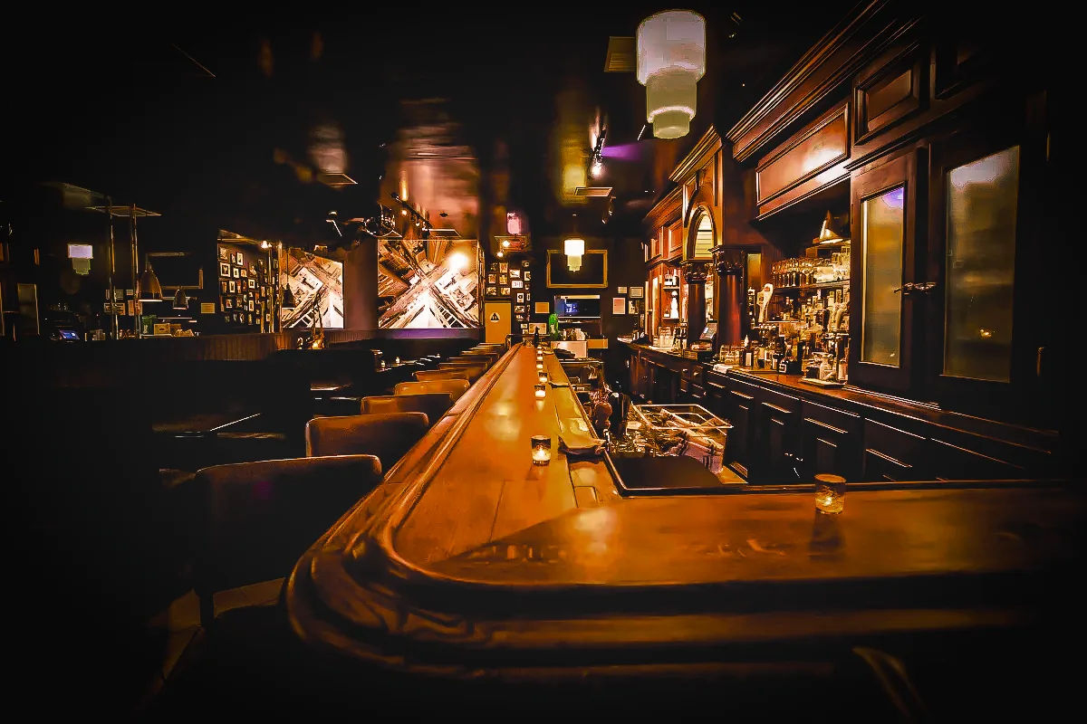 A long wooden bar with upholstered stools, paneled walls, framed pictures, and warm lighting inside Paul Bar/Food.
