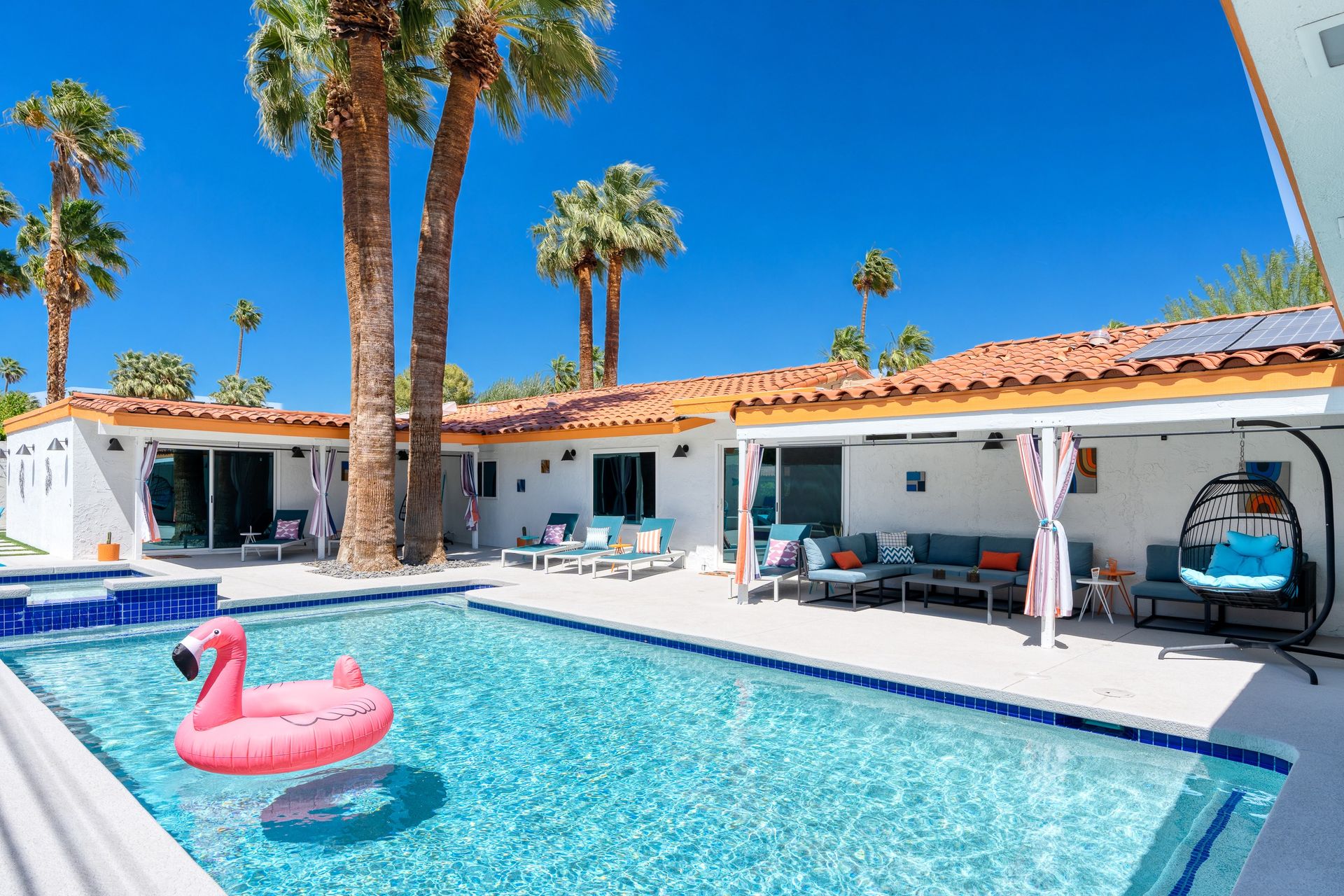 The Orchid House pool with a pink flamingo float beneath tall palms on a sunny day
