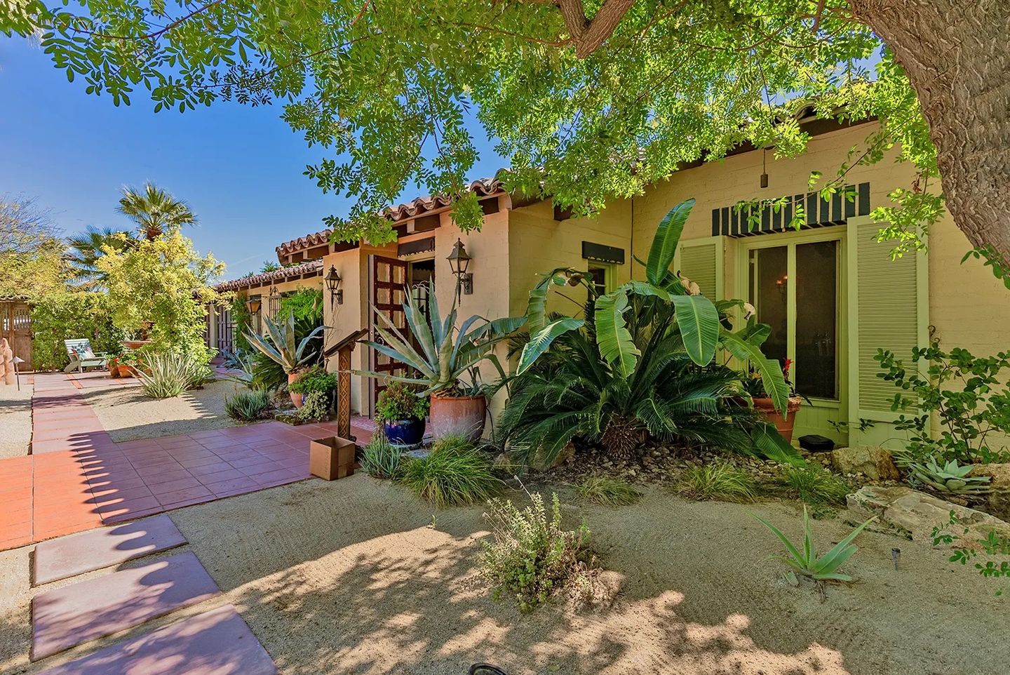 Spanish Colonial Revival garden facade of the Snyder Residence beneath mature trees, with terracotta paths and desert planting.