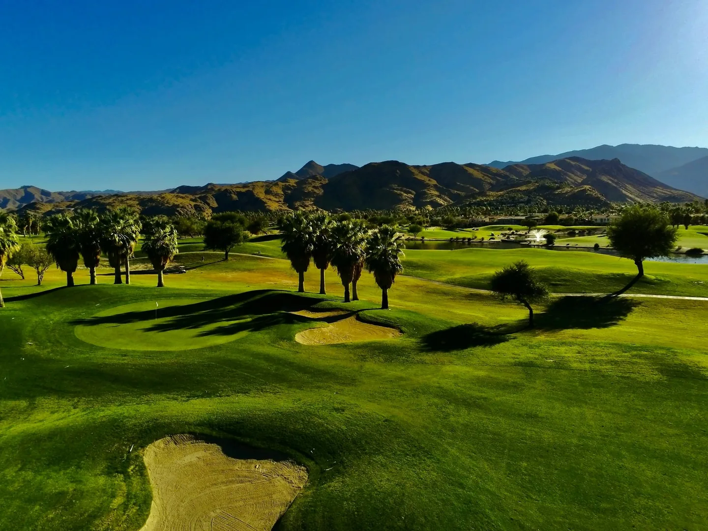 Tahquitz Creek Golf Resort fairways, palms, and a fountain below desert mountains.