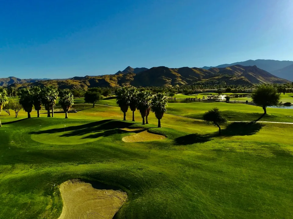 Tahquitz Creek Golf Resort fairways, palms, and a fountain below desert mountains.