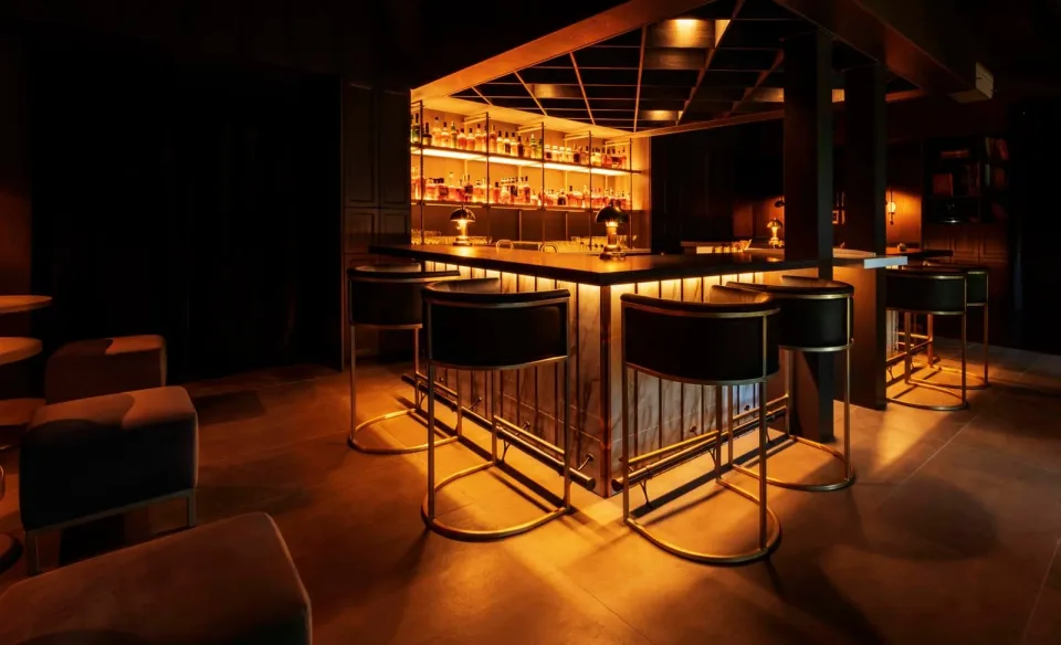 Warmly lit bar stools face a backlit wall of spirits inside Tailor Shop in Palm Springs.