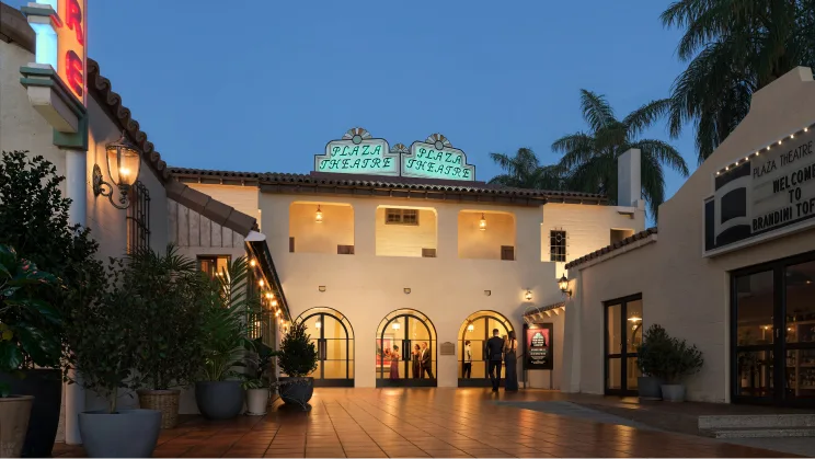 The restored Plaza Theatre courtyard at dusk, with the theatre entrance and illuminated Plaza Theatre signs.