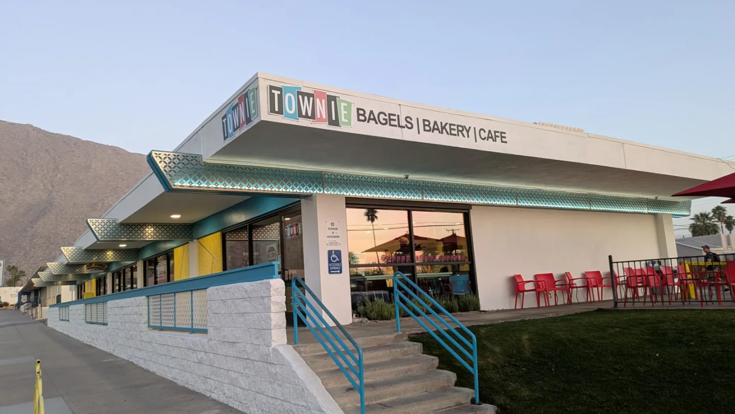 The Townie Bagels storefront has turquoise trim, red patio chairs, and mountains behind it.
