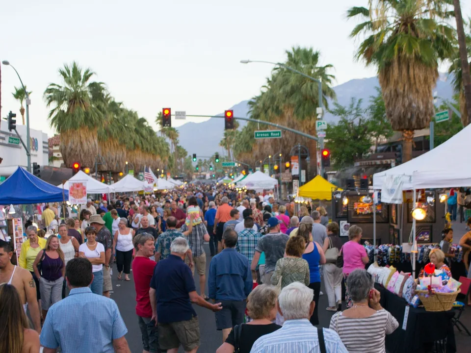 Palm Springs VillageFest fills Palm Canyon Drive with vendor tents and an evening crowd beneath palms and the San Jacinto Mountains.