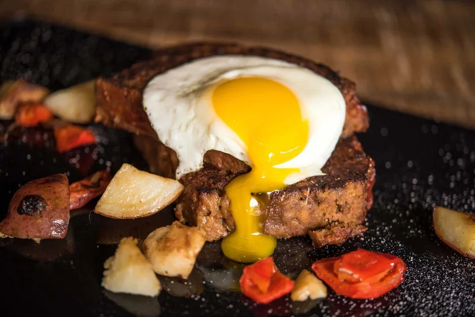 A sunny-side-up egg rests on a thick slice of griddled meatloaf with roasted breakfast potatoes.